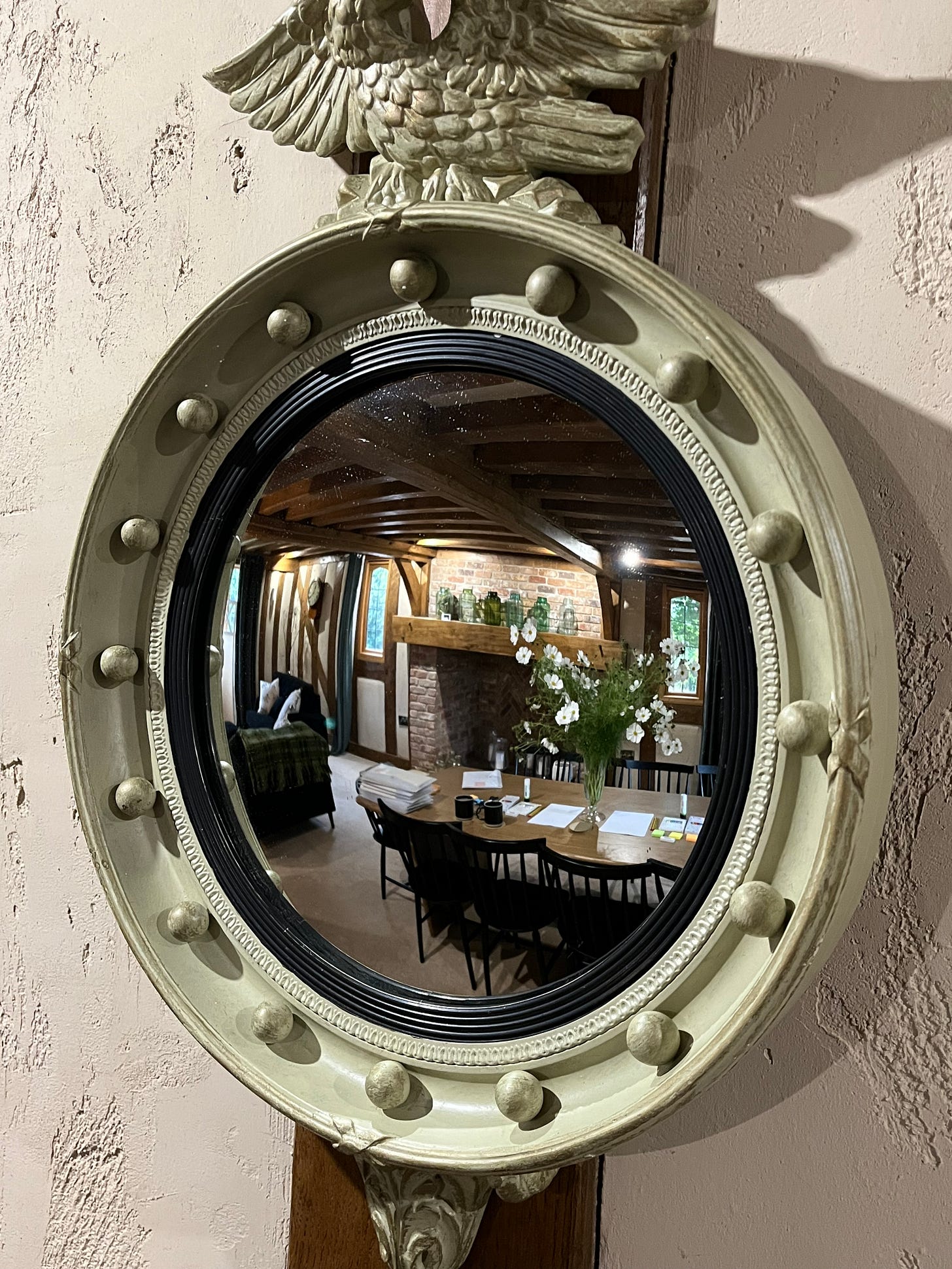 A reflection of a writing workshop taking place in a room with old wooden beams, reflected in an ornate old circular mirror with an eagle sat atop it. A reflection of a writing workshop taking place in a room with old wooden beams, reflected in an ornate old circular mirror with an eagle sat atop it.
