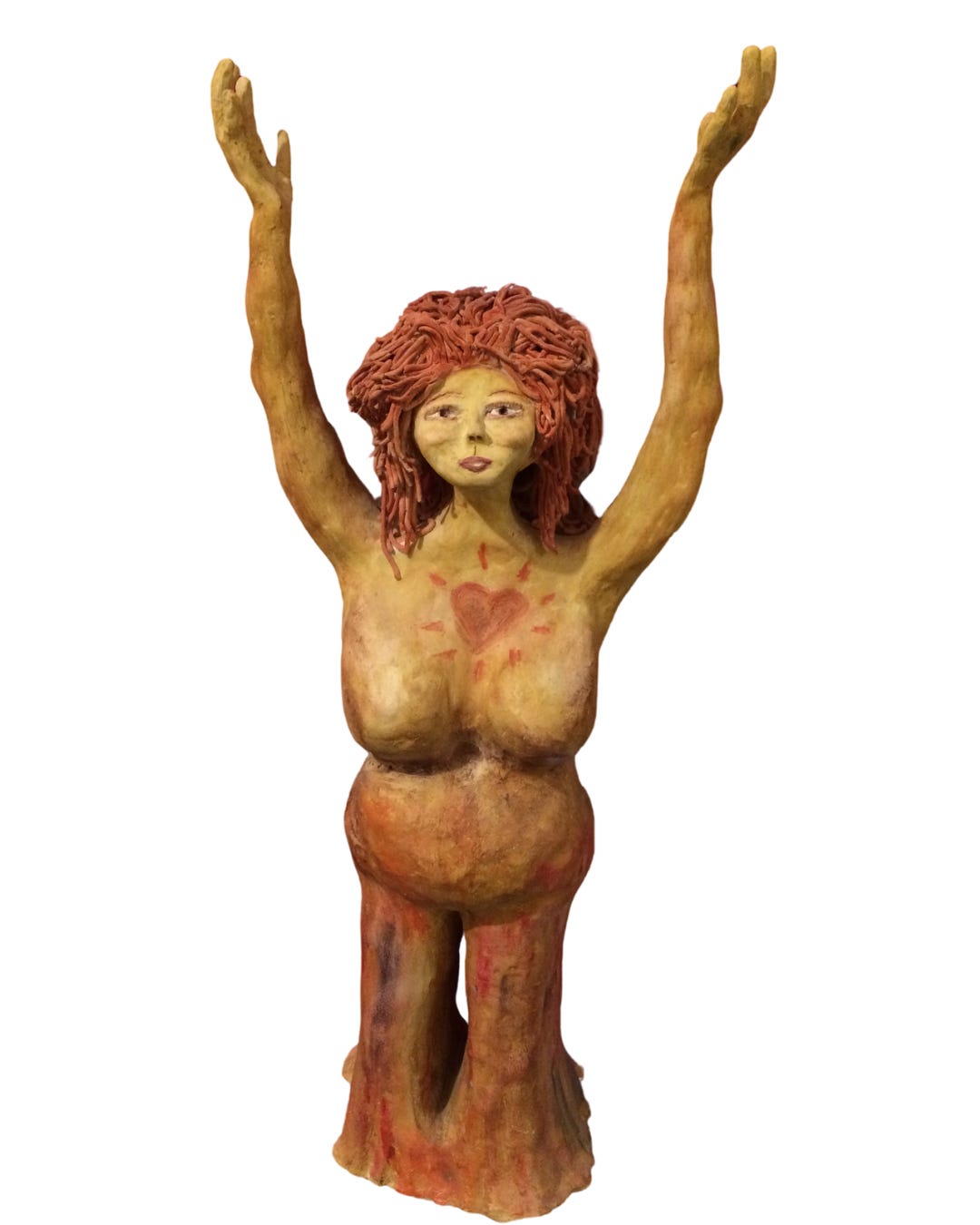 A handmade clay sculpture of a feminine figure with raised arms, kneeling with legs merging into a tree-like form. The figure has textured, flowing red hair and a serene expression on its face. The body is painted in earthy tones, with a red heart symbol on the chest surrounded by radiating lines. The sculpture has an organic, goddess-like presence, evoking themes of nature, spirituality, and empowerment.