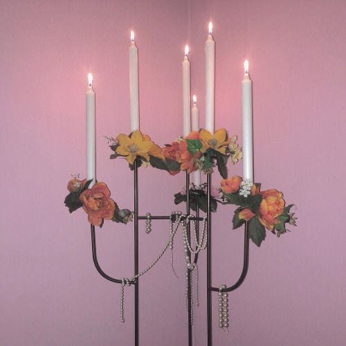 This may contain: a candle holder with five candles and flowers on the top, in front of a purple wall