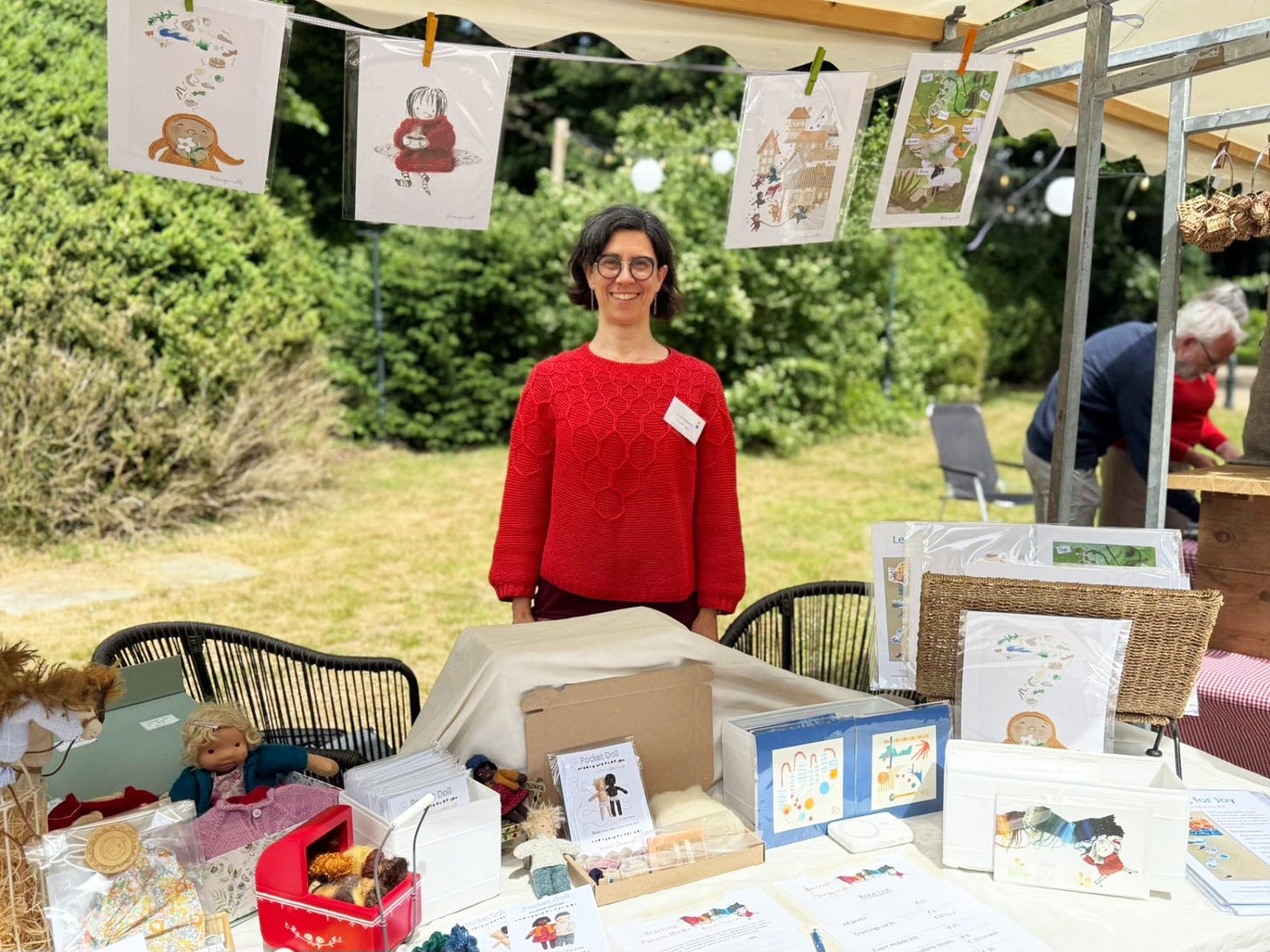 hoto of illustrator and Doll-Maker Hannah Sanguinetti smiling and standing behind a market stall selling her illustrations and doll-making kits.