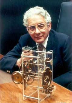 Derek de Solla Price wearing glasses and sitting in a chair with a metal device. Derek de Solla Price wearing glasses and sitting in a chair with a metal device.