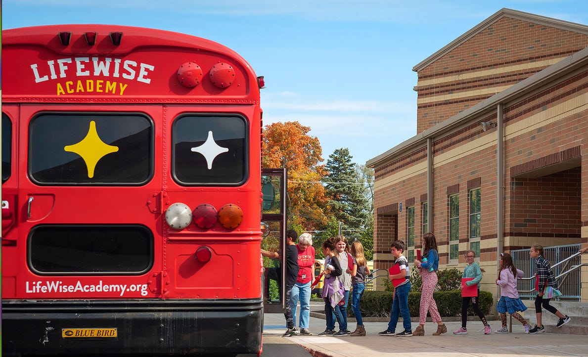 Red school bus from LifeWise Academy picking up students at an elementary school