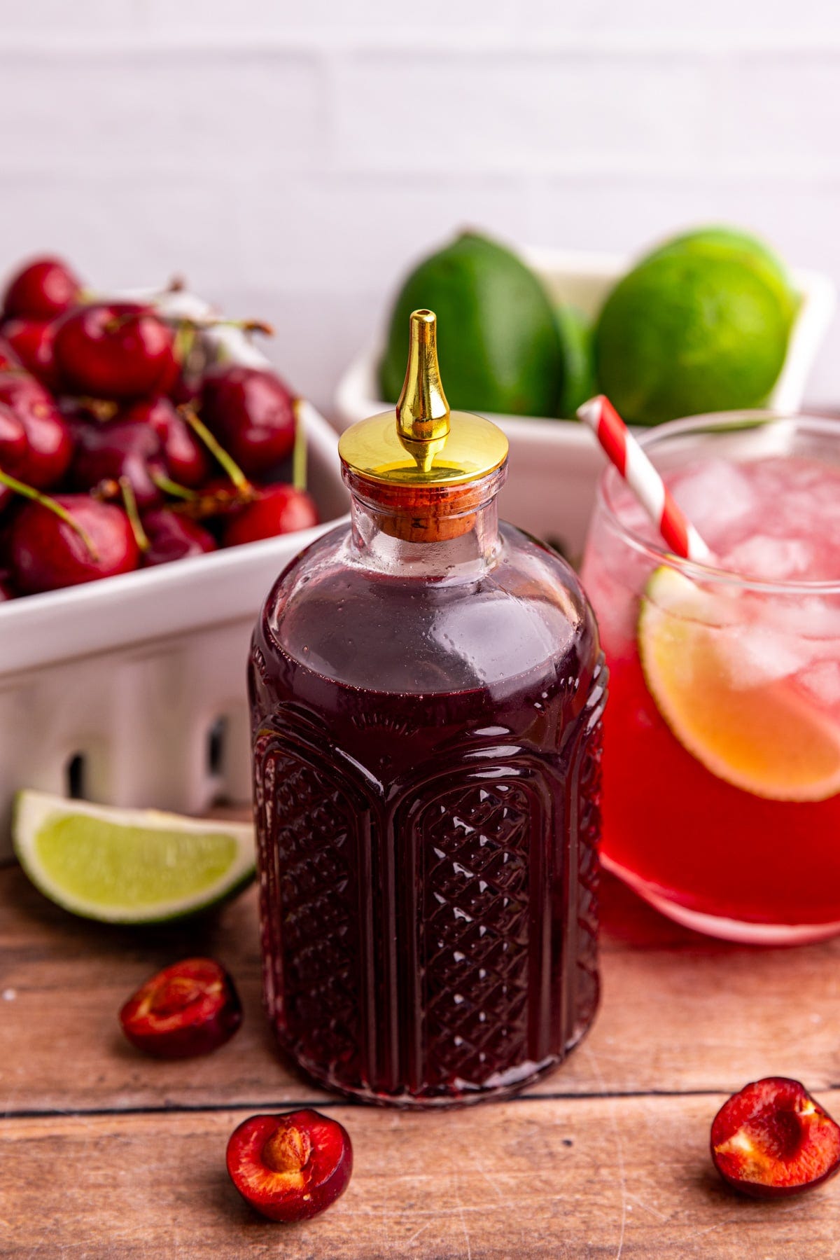 A bottle of cherry simple syrup, with fresh cherries and limes.