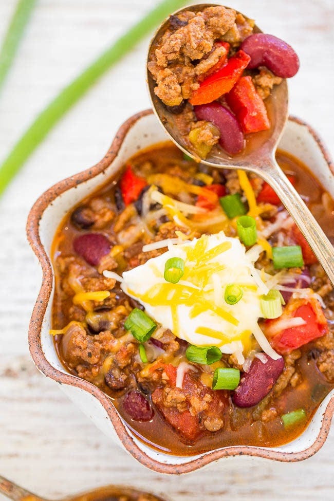 A spoon holding a bite of slow cooker beef chili over a bowl. 