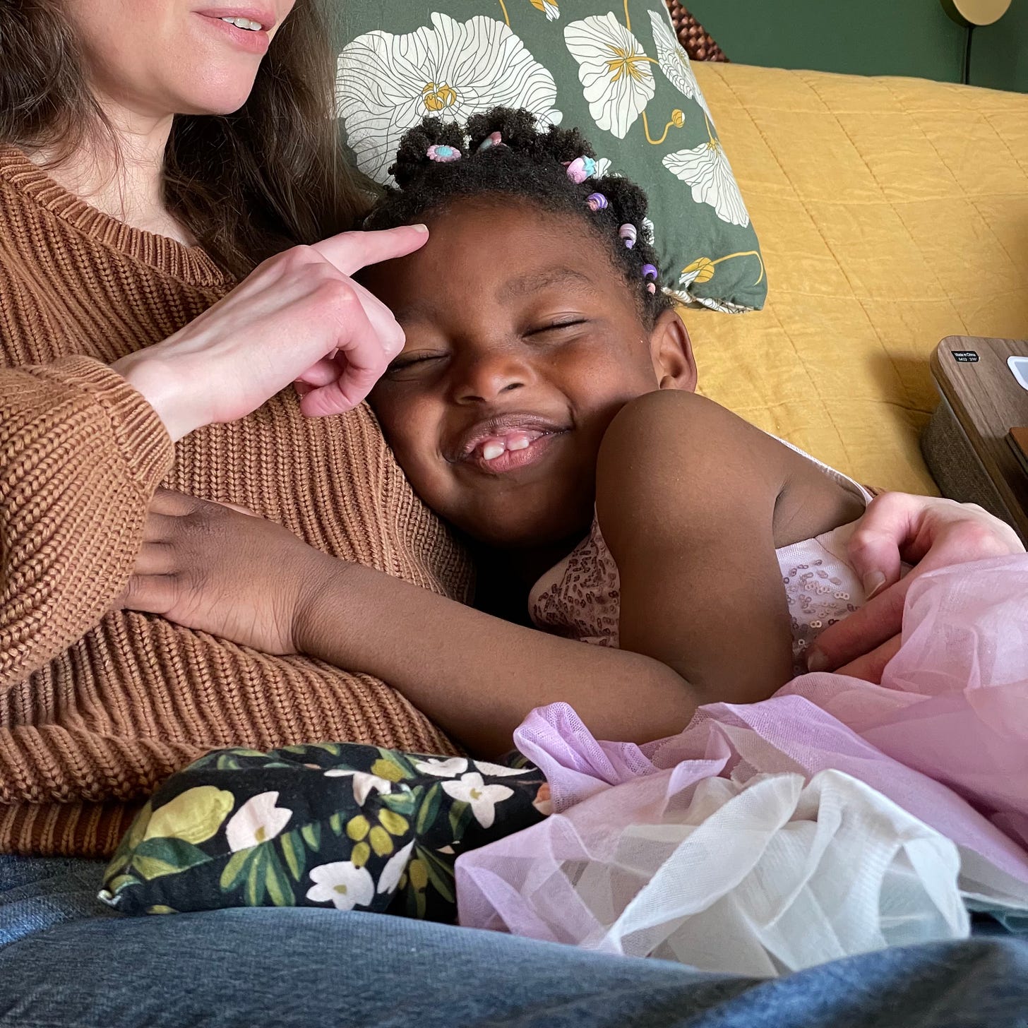 a kid in a pink dress grinning as they cuddle