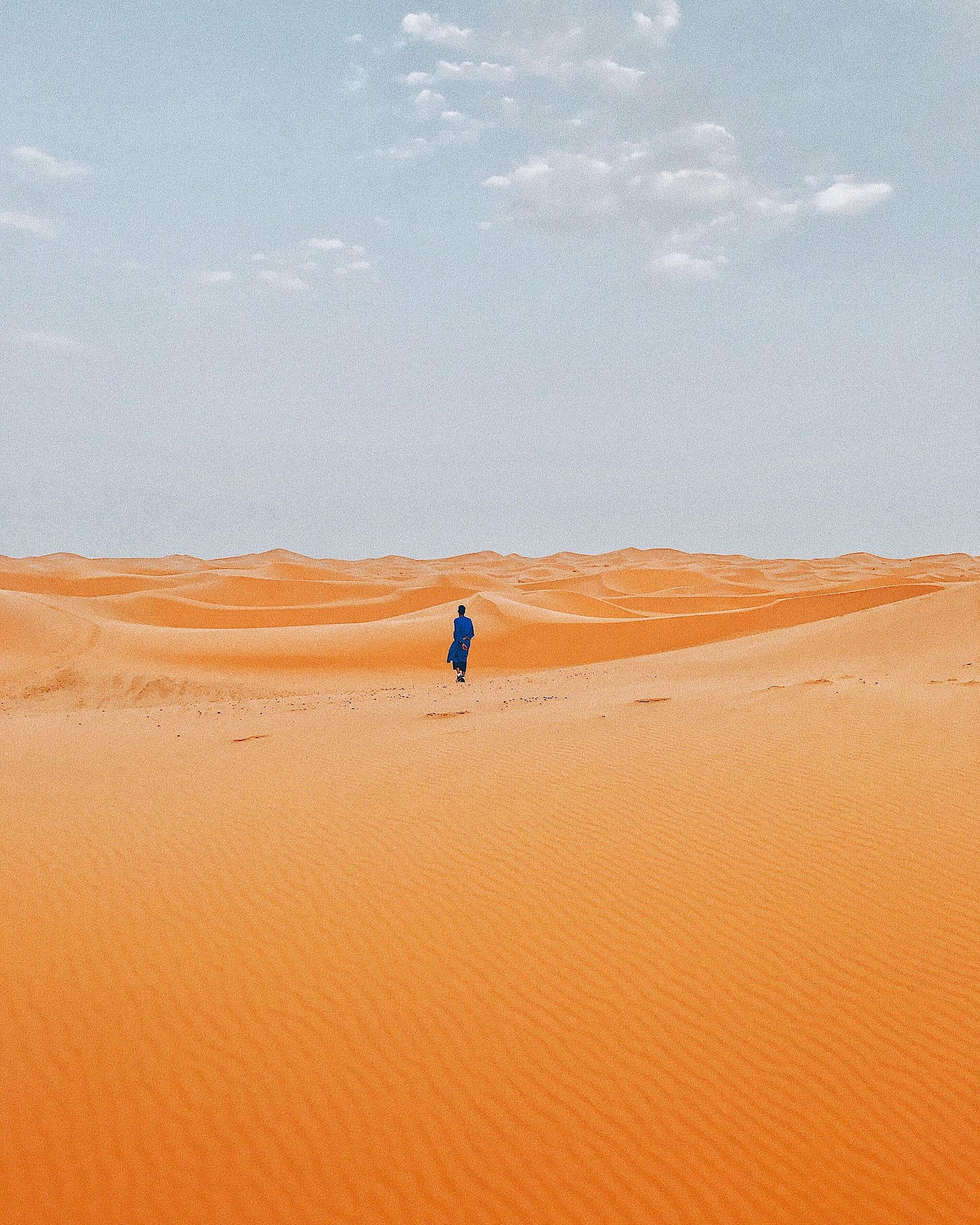 Male human figure striding across wide sand dunes under a clear blue sky