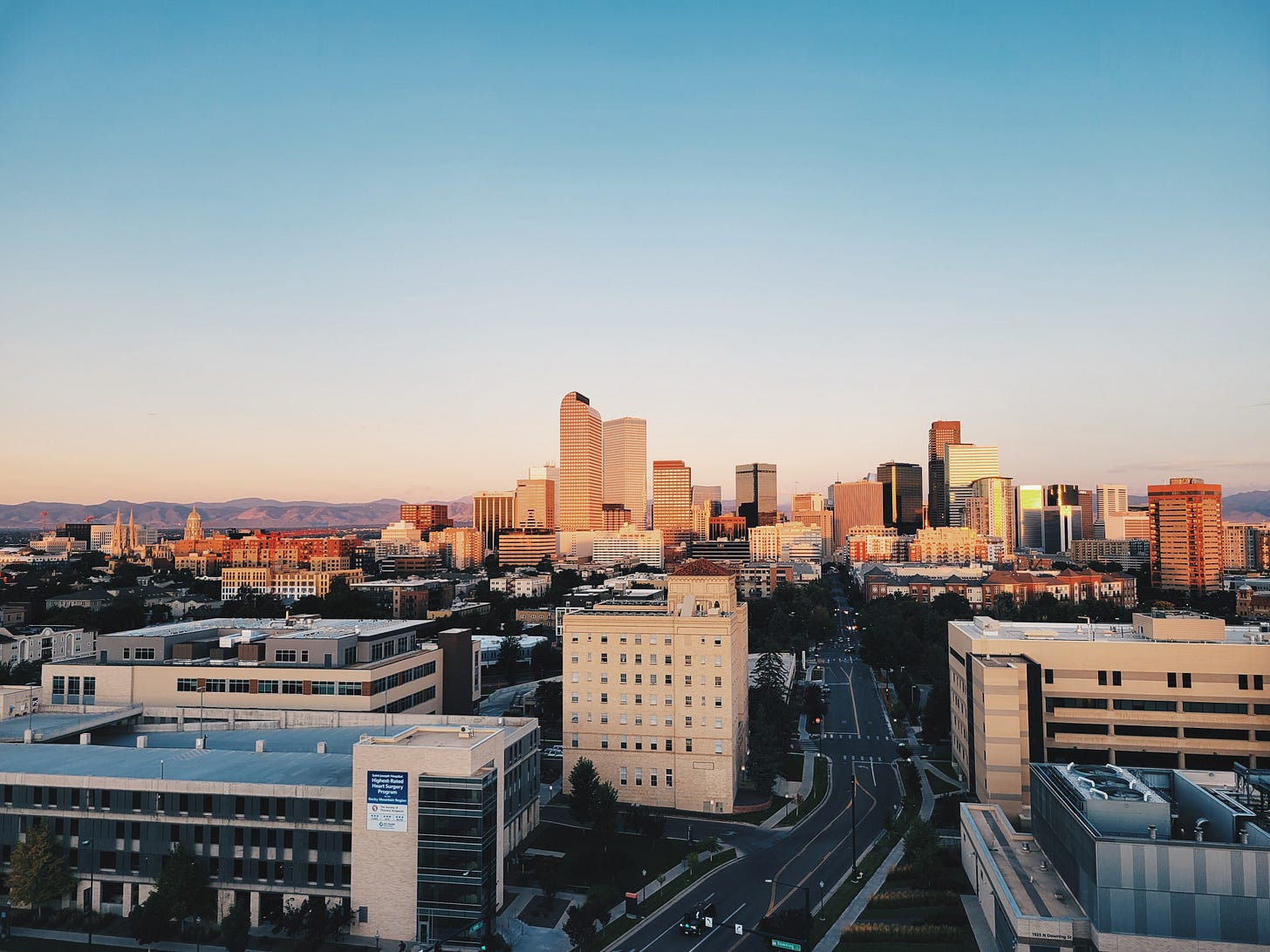 Denver skyline at sunset with Rocky Mountains visible in background, downtown buildings lit by golden hour light Denver skyline at sunset with Rocky Mountains visible in background, downtown buildings lit by golden hour light