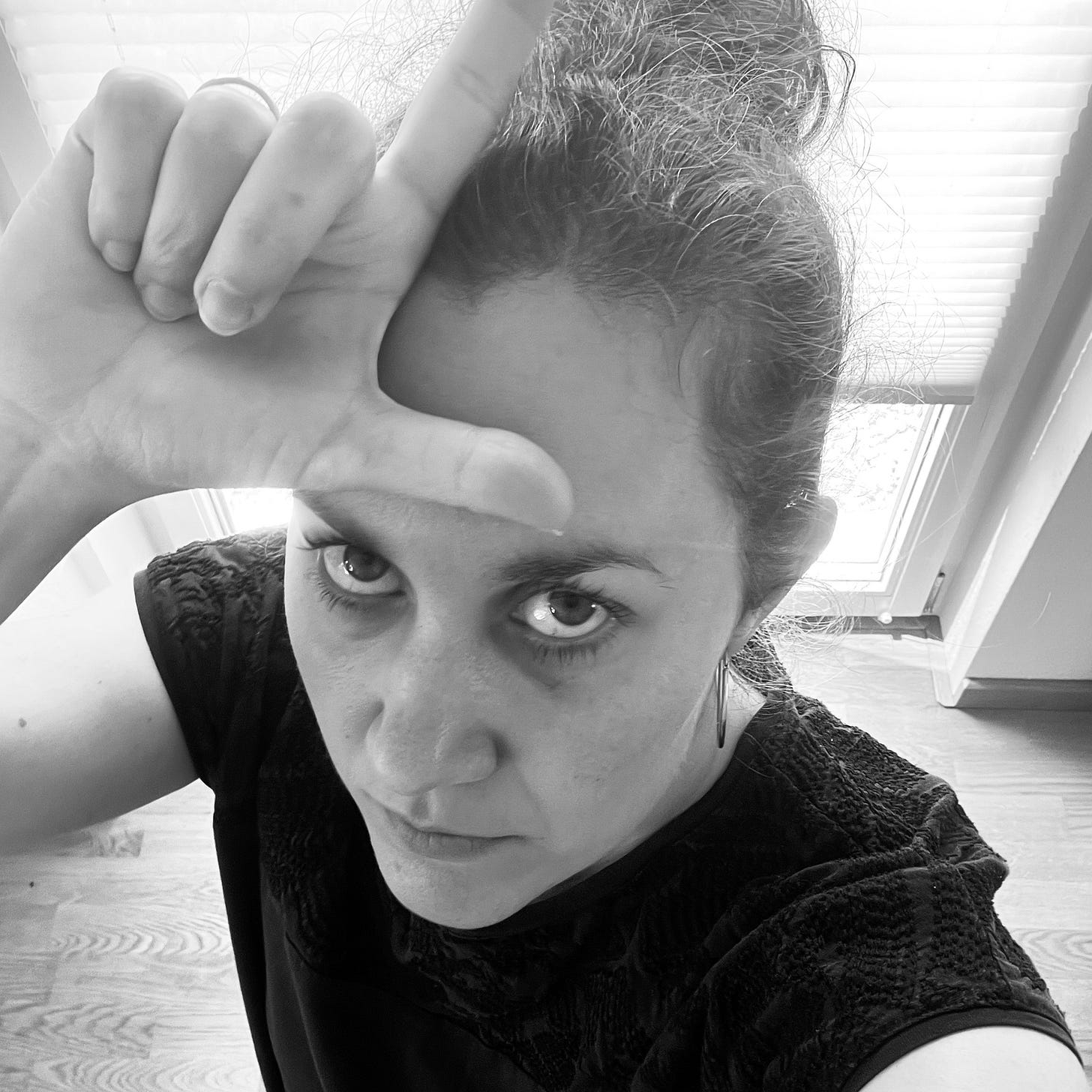 Selfie. Miriam schaut in die Kamera und hält ihre Finger wie ein L geformt über ihrer Stirn.