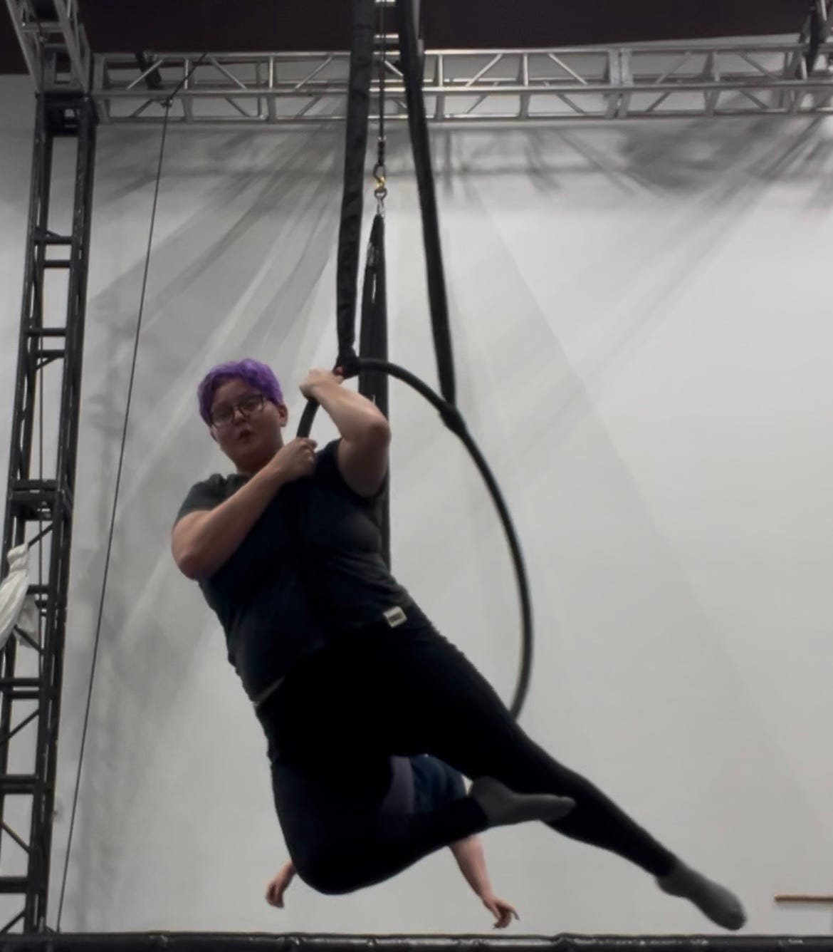 mayson, a nonbinary person with short purple hair and square black glasses, hangs from a lyra