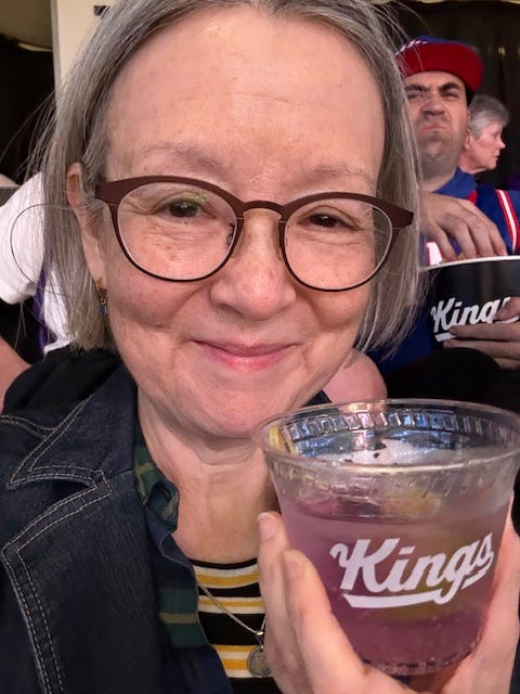 Woman holding plastic drink cup with "Kings" written on it. Drink is purple. A man behind her is scowling Woman holding plastic drink cup with "Kings" written on it. Drink is purple. A man behind her is scowling