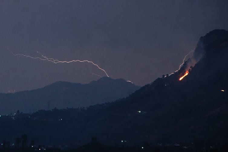 Lightning strikes behind a mountain as smoke bellows from a wildfire in the foreground. Lightning strikes behind a mountain as smoke bellows from a wildfire in the foreground.