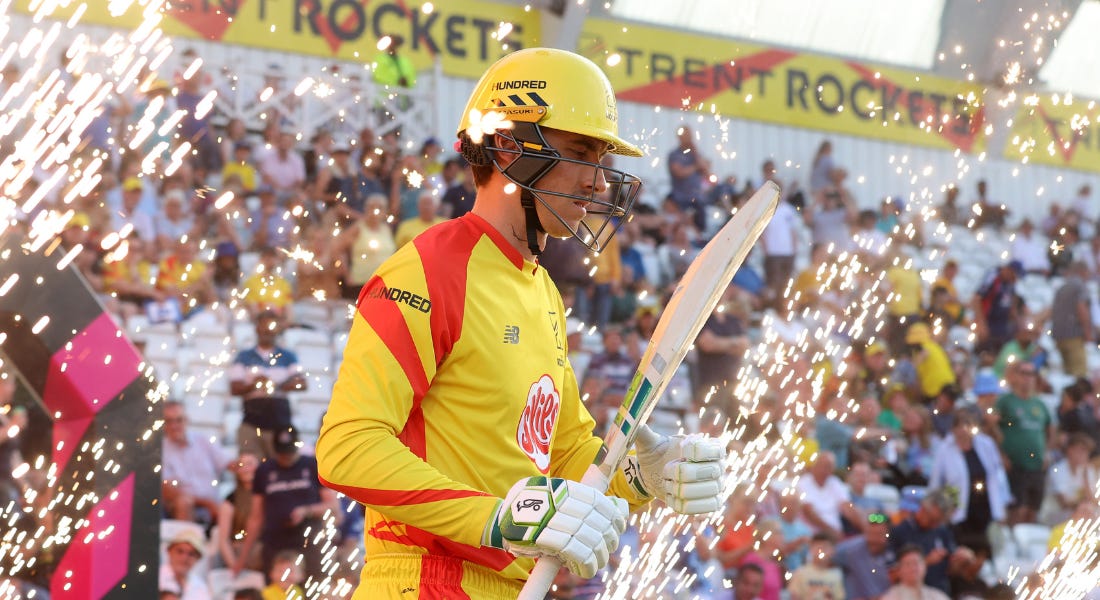 A Trent Rockets cricket player walking with fireworks around them and a crowd in the stands behind them A Trent Rockets cricket player walking with fireworks around them and a crowd in the stands behind them