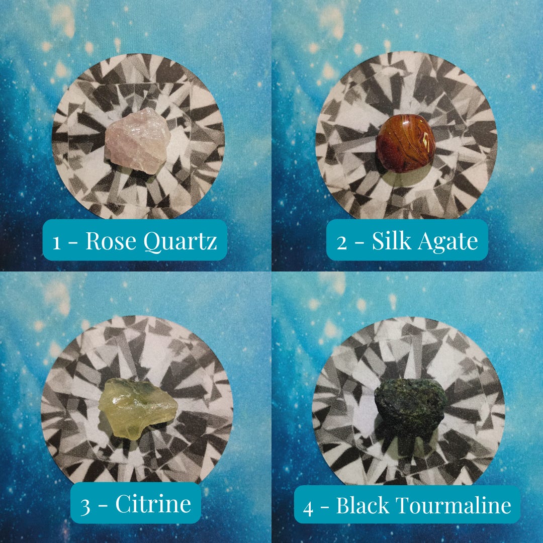Crystals and face-down cards on a starry blue background. Pile 1 - Rose Quartz (pink), Pile 2 - Silk Agate (Orange and brown), Pile 3 - Citrine (yellow), Pile 4 - Black Tourmaline