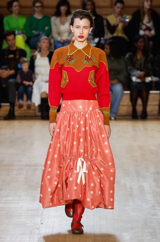 A person wearing a red sweater and a long skirt

Description automatically generated
