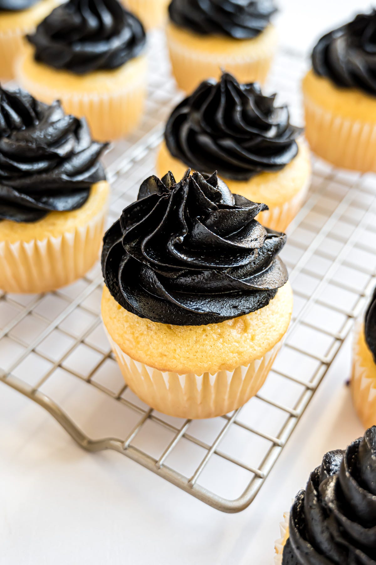 A yellow cupcake topped with a swirl of piped black frosting.