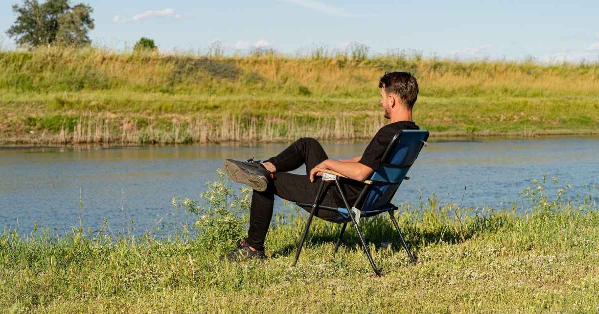 A man in casual attire enjoys a peaceful moment sitting by a tranquil river