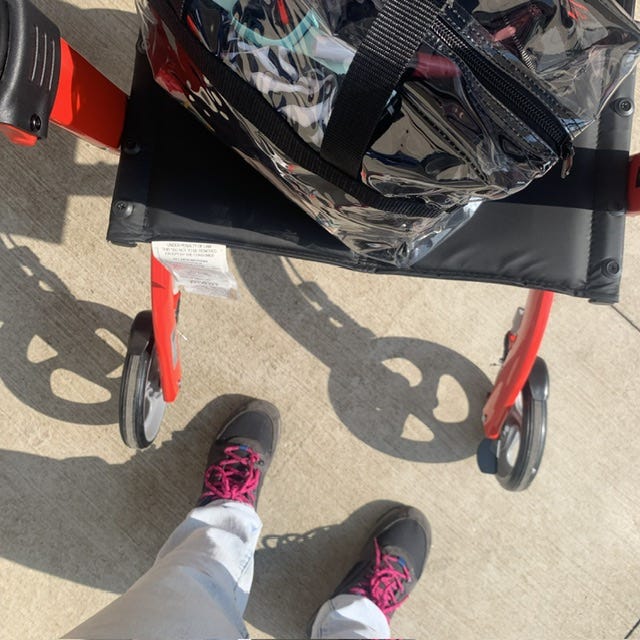 Close up of sneakers, red rollator, and clear bag, waiting to enter the club section 