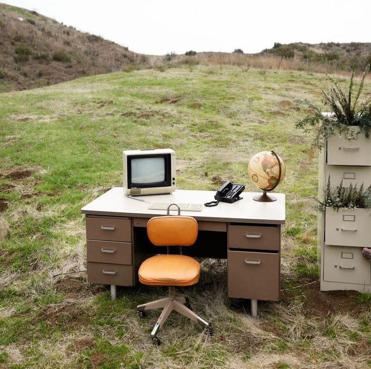 Escritório vintage ao ar livre, com mesa, cadeira laranja, computador antigo, telefone, globo e arquivos com plantas, em um campo gramado