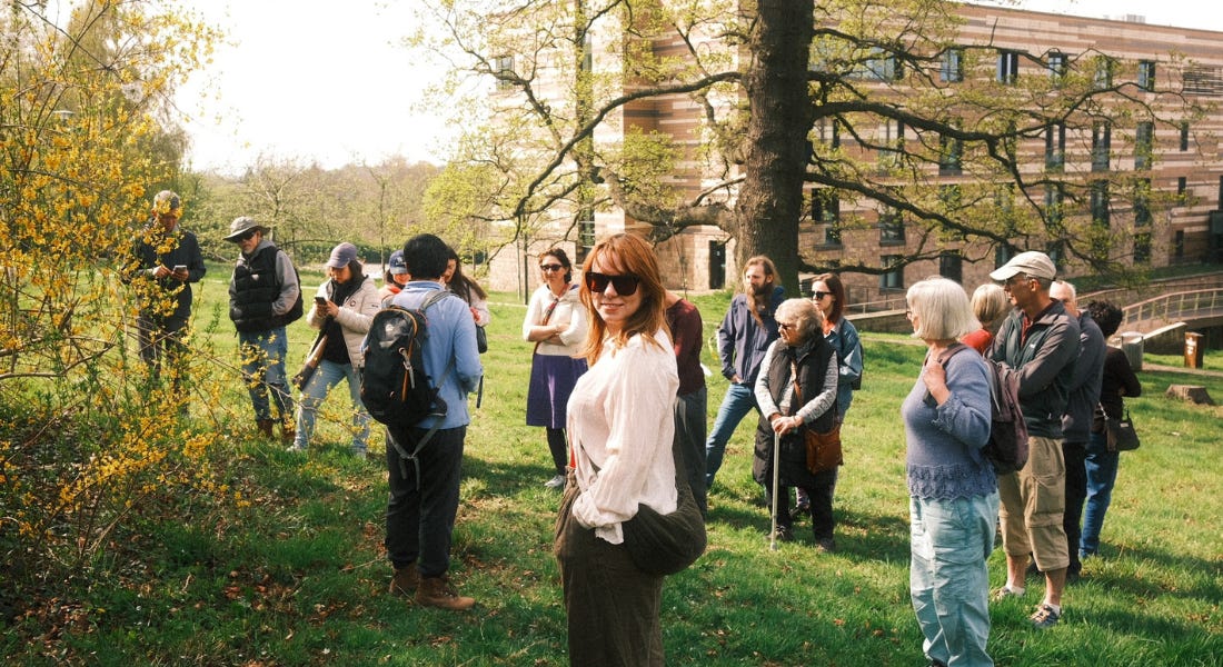 A group of people standing on a field foraging at the University of Nottingham, with a building in the background