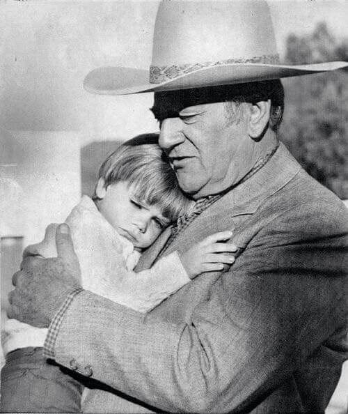 This may contain: an old man in a cowboy hat hugging a young boy with his arms around him