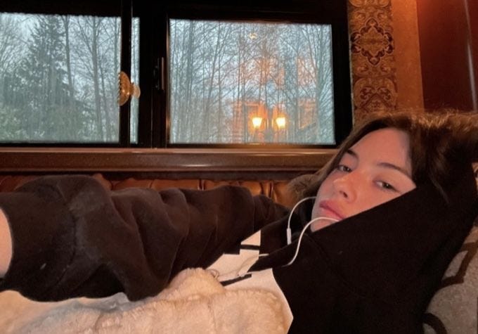 This may contain: a woman laying on top of a bed with headphones in her ears next to a window