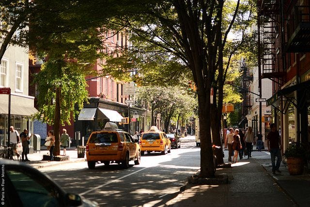 This may contain: people are walking down the street in front of taxi cabs and trees on a sunny day