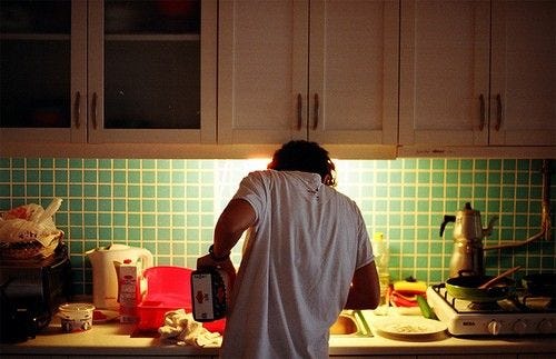 This may contain: a person standing in a kitchen with green tiles on the wall and counter top, holding a blender