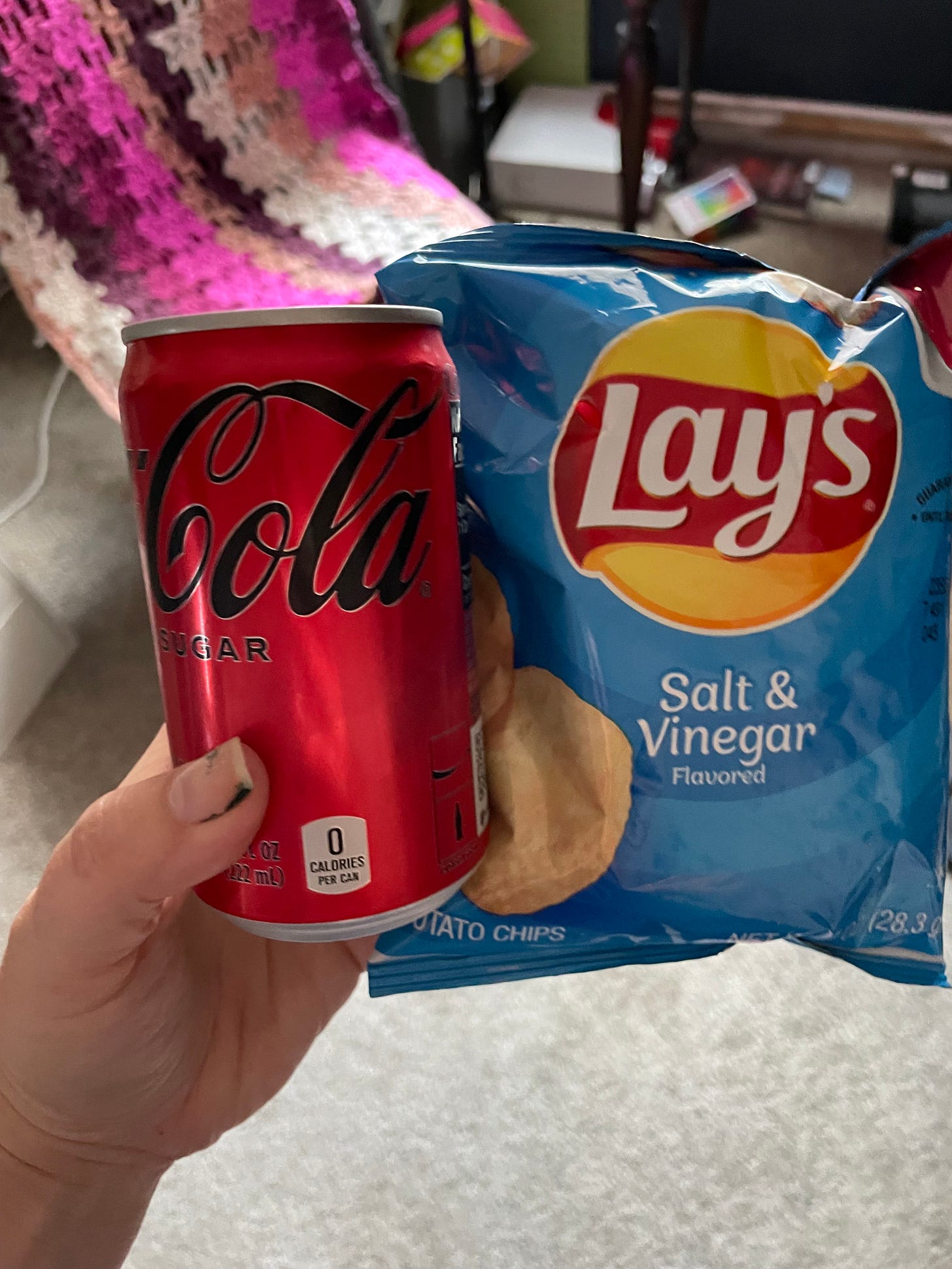 a white hand holds up a tiny can of coke zero and a small bag of vinegar and sea salt chips