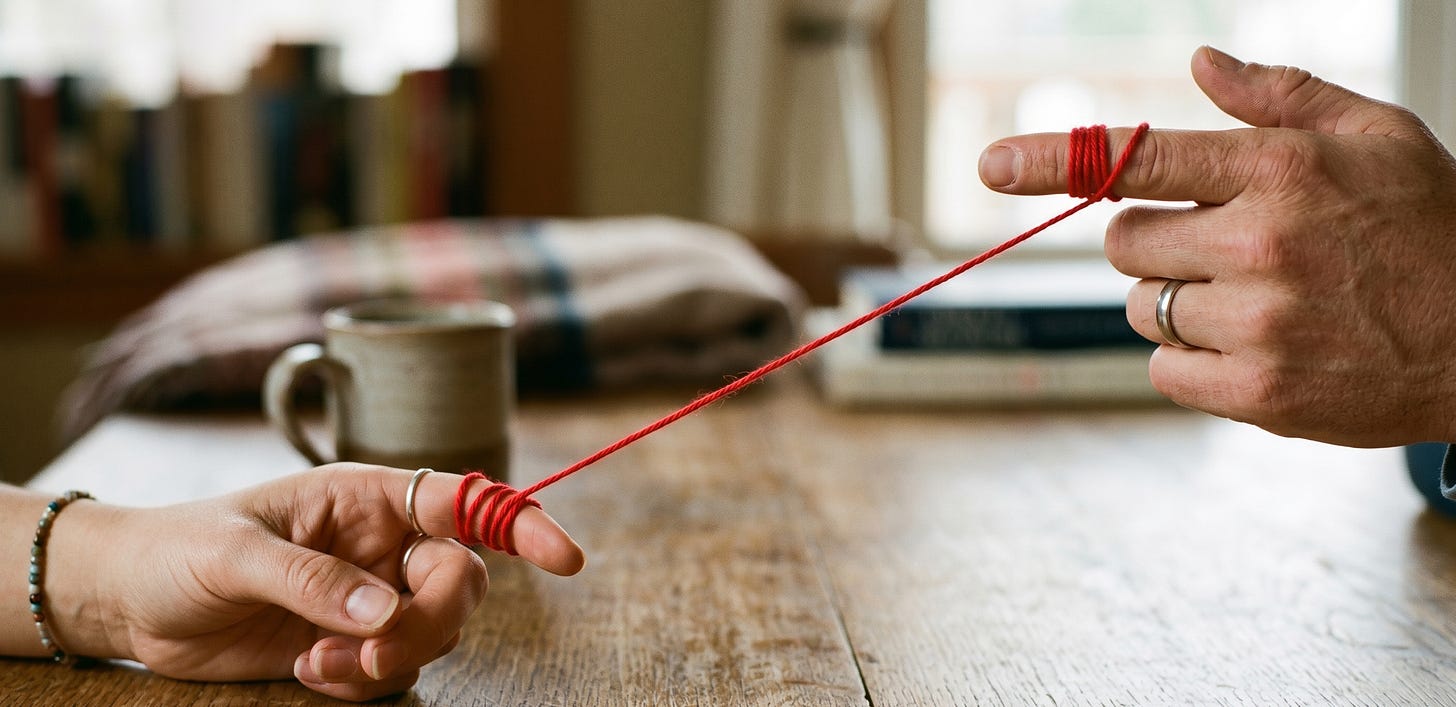 There are two hands linked by a red thread across a table.