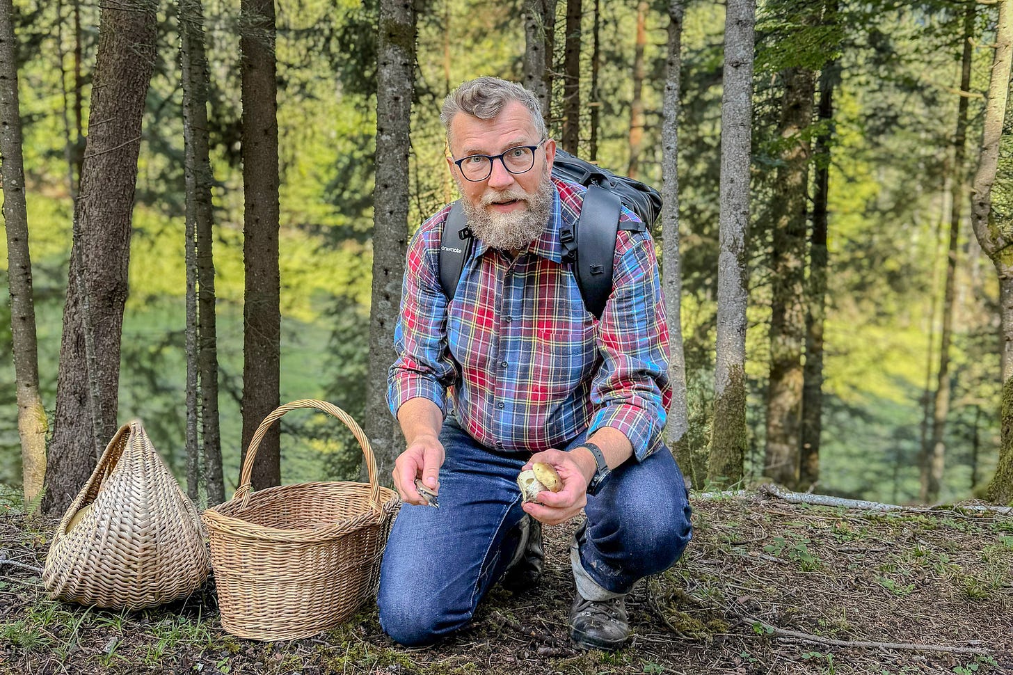 Der Agrarjournalist Jürg Vollmer – ein bärtiger Mann im karierten Hemd, Jeans und Wanderschuhen – kniet im Wald neben einem Pilzkorb. Er trägt einen Rucksack und hält einen frisch gefundenen kleinen Steinpilz in der Hand, den er direkt an der Fundstelle mit einem Messer putzt. Im Hintergrund sind Bäume und grünes Waldlicht zu sehen. Der Agrarjournalist Jürg Vollmer – ein bärtiger Mann im karierten Hemd, Jeans und Wanderschuhen – kniet im Wald neben einem Pilzkorb. Er trägt einen Rucksack und hält einen frisch gefundenen kleinen Steinpilz in der Hand, den er direkt an der Fundstelle mit einem Messer putzt. Im Hintergrund sind Bäume und grünes Waldlicht zu sehen.