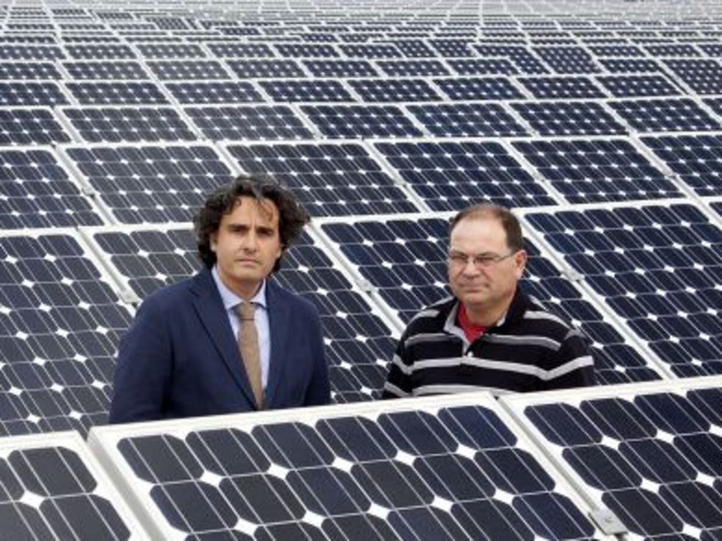 Two men stand amid an extensive solar panel farm, symbolizing the human and financial impact of Spain's solar energy crisis