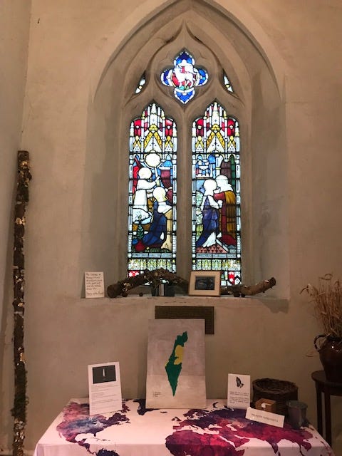 text of a prayer for those suffering in the Israeli-Palestine conflict today and also for us; second image includes the background of the stained glass window above the table with a tablecloth showing a map of the world in pink and white and a map of the Gaza strip and surrounding area including Jerusalem and Bethlehem