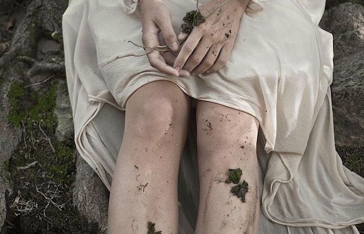 This may contain: a woman sitting on top of a rock covered in mud and dirt with her hands over her knees