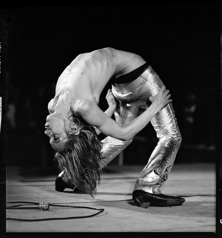 This may contain: a man in metallic pants is doing a handstand on the floor with his head down