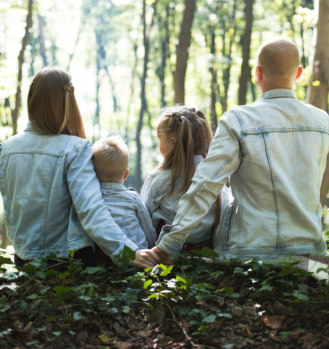 man and woman holding hands together with boy and girl looking at green trees during day