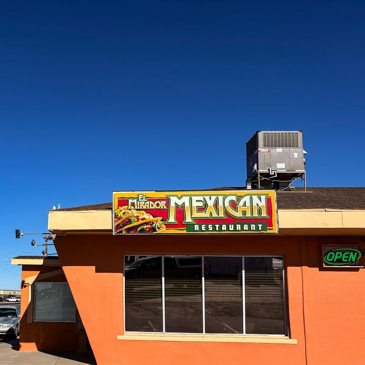 Coral colored cement building with Mexican Restaurant sign and adobe building with Historic Place sign