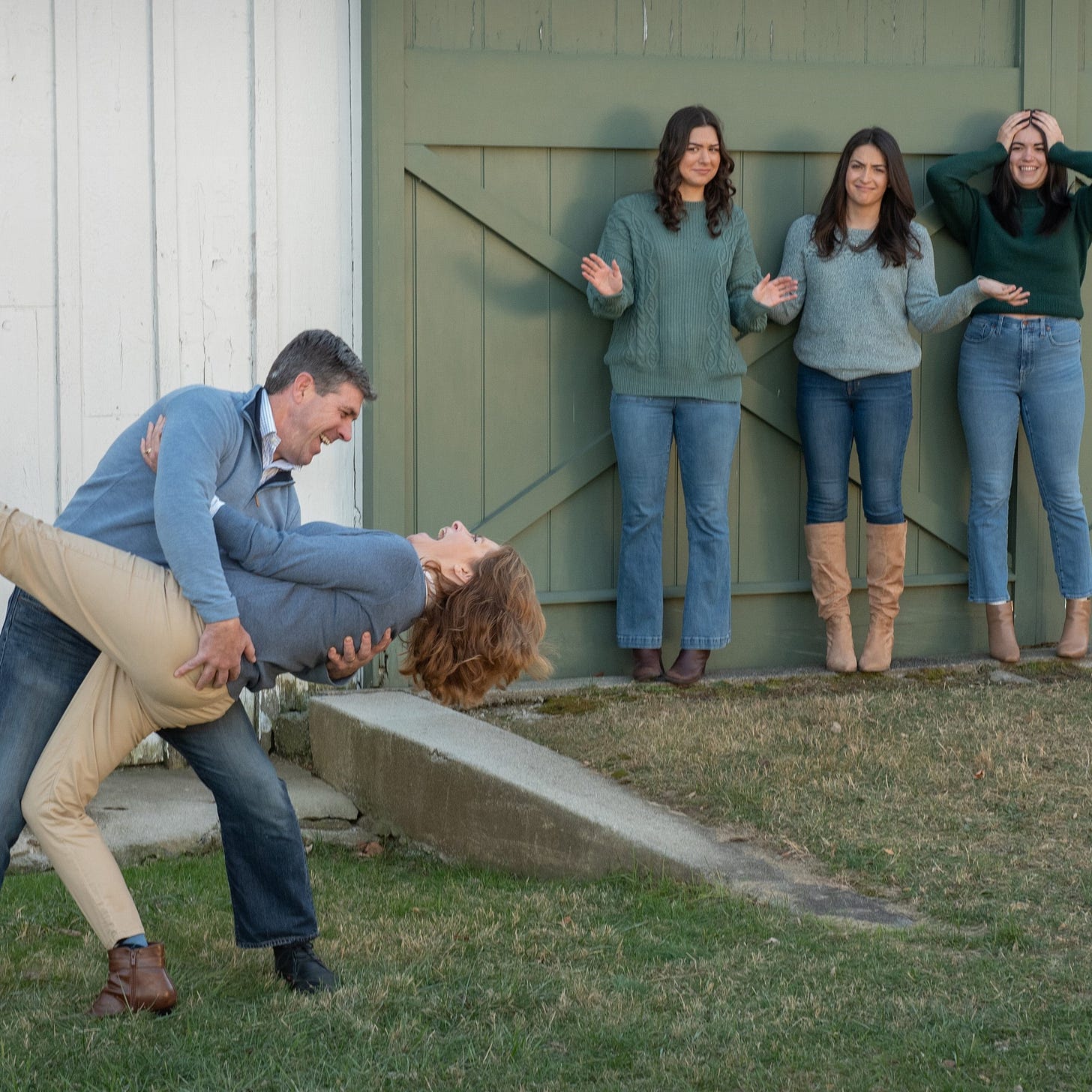 Dad and mom look exhilarated after dad dips mom backwards as they pose for a family portrait. Their three grown children look on, aghast. Dad and mom look exhilarated after dad dips mom backwards as they pose for a family portrait. Their three grown children look on, aghast.
