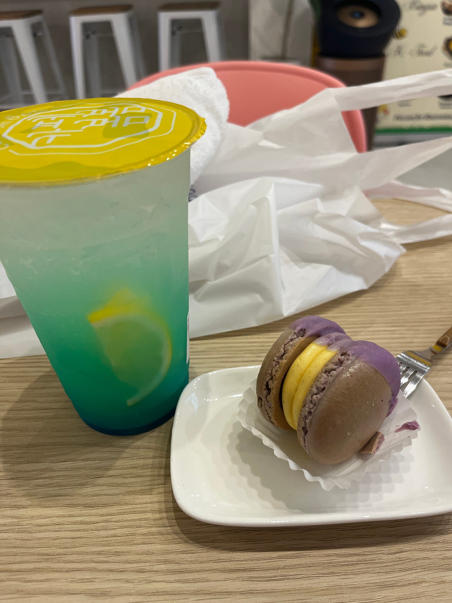 A blue lemon soda and a macaron on a wooden cafe table. 