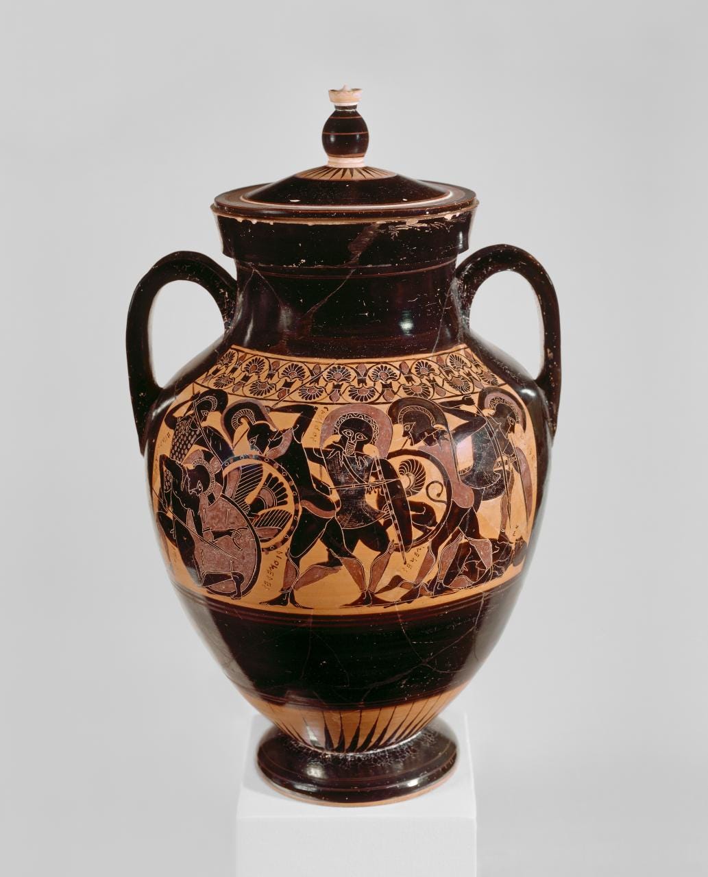 Red figure vase: Side A: Scene of fighting from the Trojan War; Achilles dismounts from his chariot to kill the fallen Eurymachus. Side B: Scenes of fighting from the Trojan War, with Glaucus (frontal, centre) and Menestheus. Subsidiary decoration: rays from the base and a lotus/palmette band above the panel. Much added red and white for details. There are holes at the base of the handles and a channel/drain hole in the base, suggesting the vessel was used for cooling wine. Red figure vase: Side A: Scene of fighting from the Trojan War; Achilles dismounts from his chariot to kill the fallen Eurymachus. Side B: Scenes of fighting from the Trojan War, with Glaucus (frontal, centre) and Menestheus. Subsidiary decoration: rays from the base and a lotus/palmette band above the panel. Much added red and white for details. There are holes at the base of the handles and a channel/drain hole in the base, suggesting the vessel was used for cooling wine.