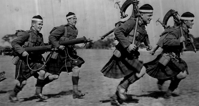 Four men in kilts and military uniforms run while carrying machine guns. Four men in kilts and military uniforms run while carrying machine guns.