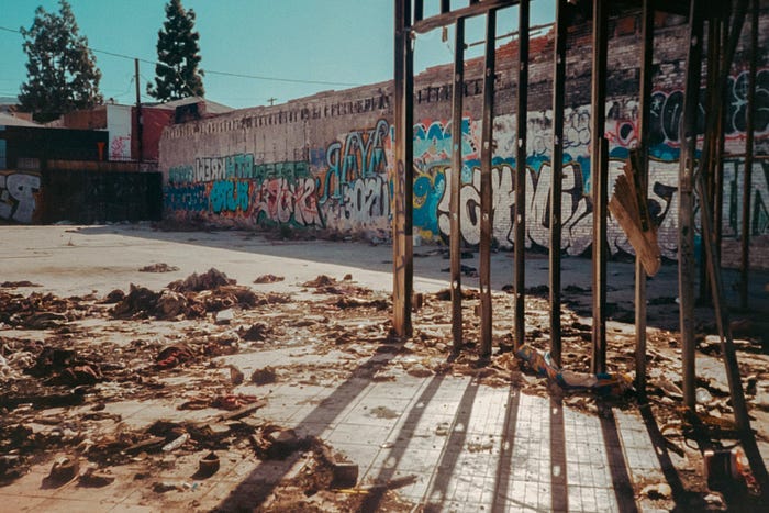 Photography of an open gate leading into a trash-strewn lot with graffiti on the walls. Photography of an open gate leading into a trash-strewn lot with graffiti on the walls.