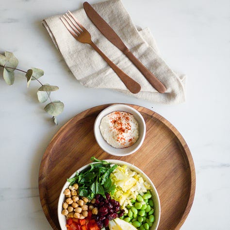 Chickpea-Edamame Salad served in a bowl with fresh spinach, romaine, cucumber, bell pepper, and a creamy hummus dressing.