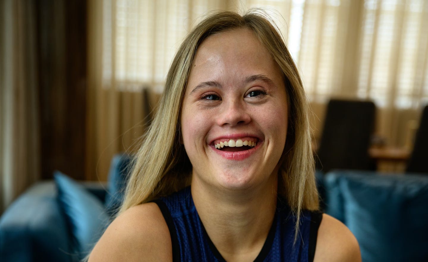 A white woman with Down syndrome smiles widely in a photo at home.