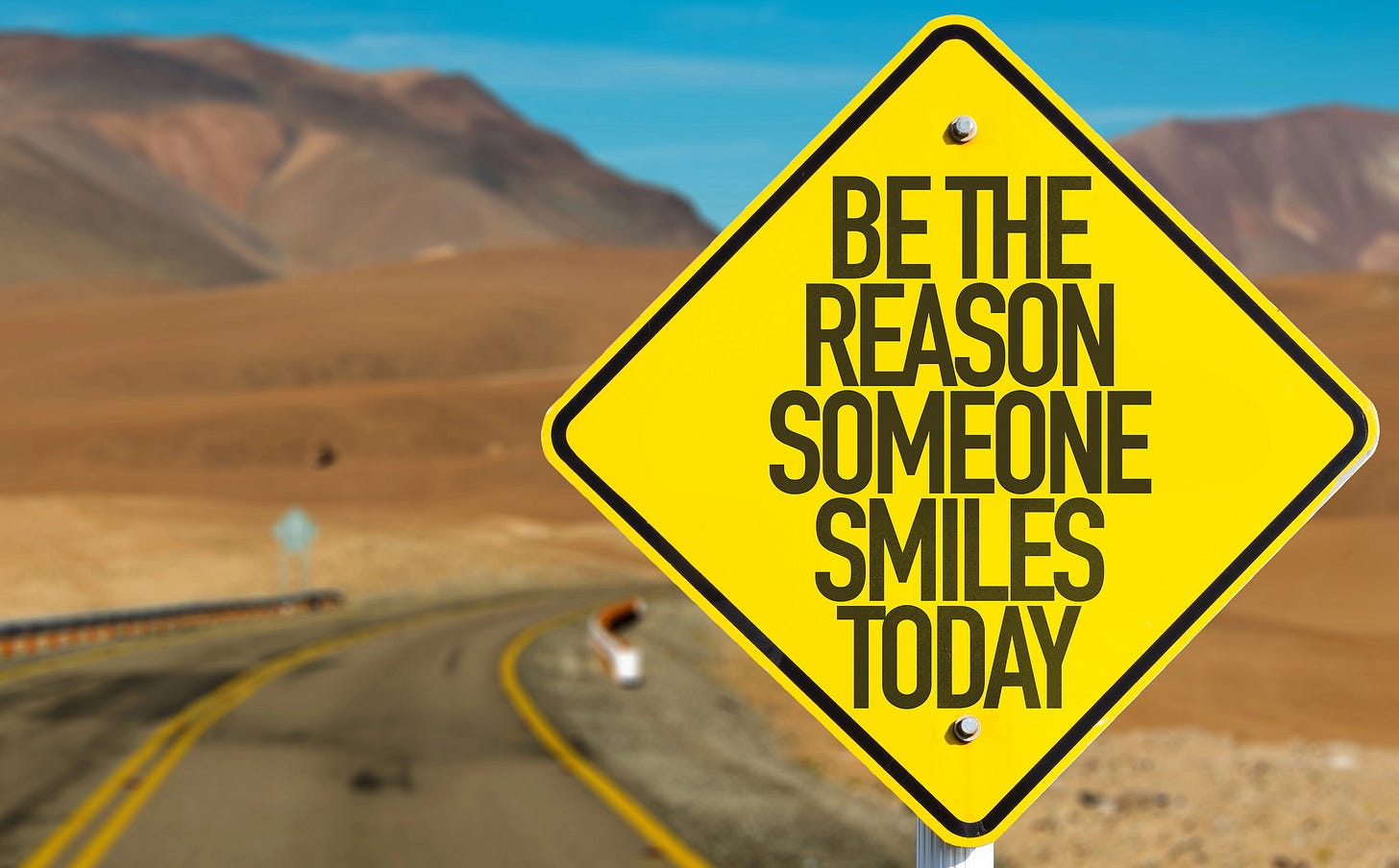 A highway with a road sign that reads "Be the reason someone smiles today"