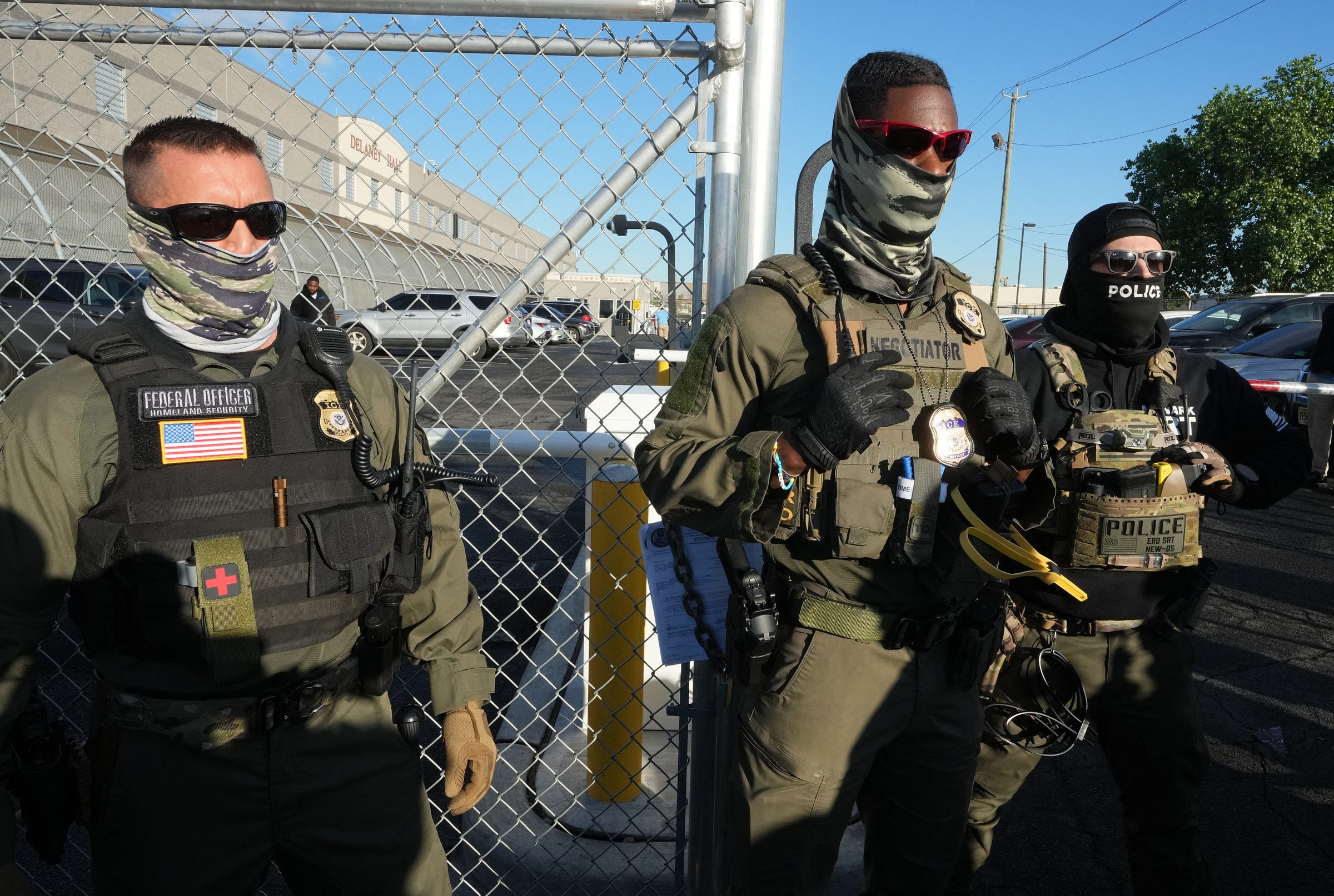 Three masked ICE agents stand in front of fence Three masked ICE agents stand in front of fence