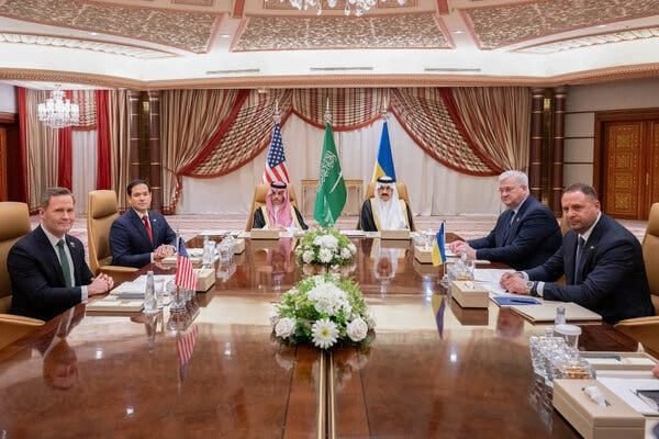Men in suits seated around a wooden conference table. 