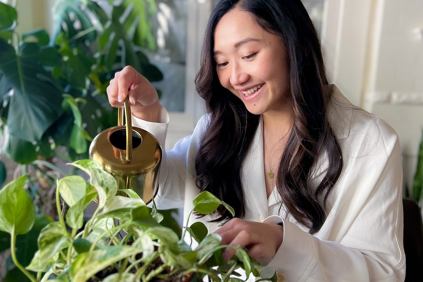 Woman with long brown hair watering plants with a a gold watering can