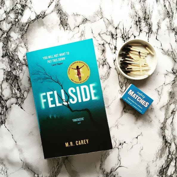 Paperback of Fellside by M.R. Carey next to a box of matches.