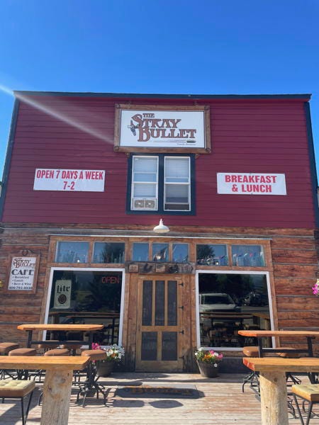 Front of a rustic-looking building with a bright blue sky behind. Sign on front says The Stray Bullet, Breakfast and Lunch