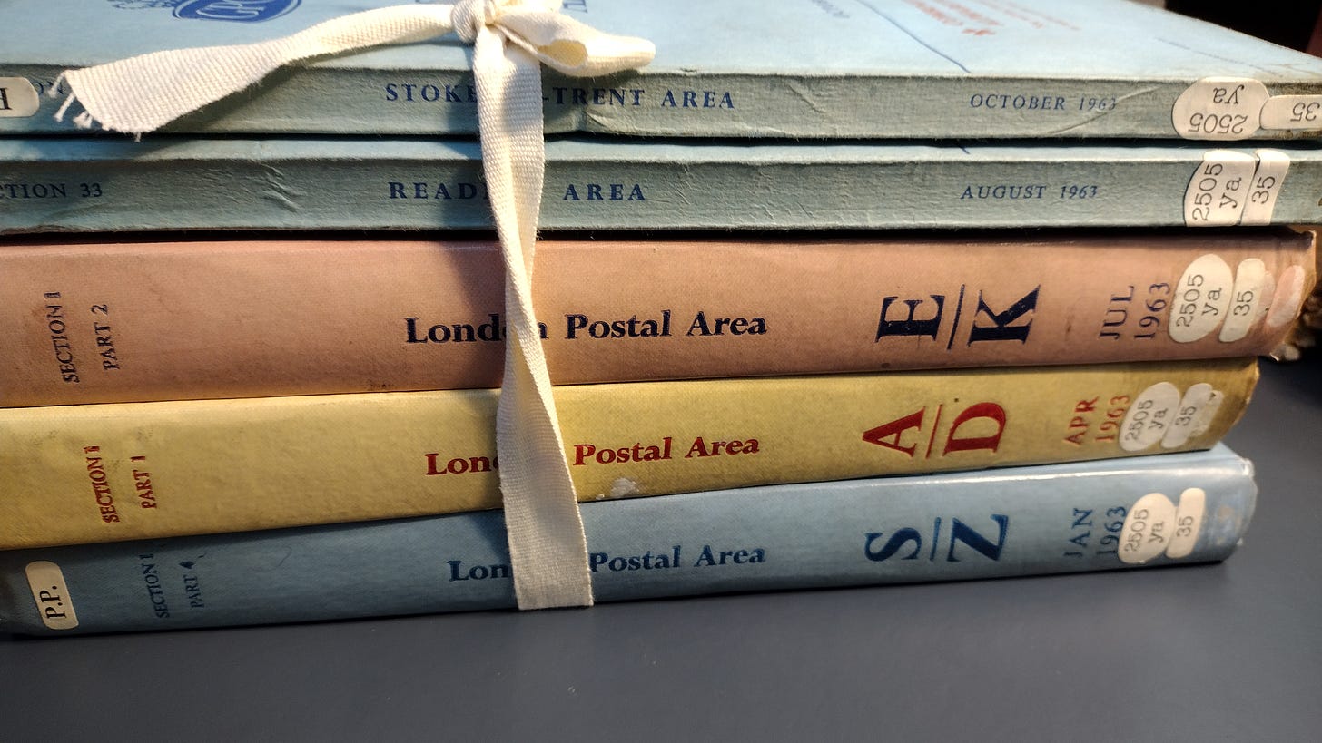 Three of the four volumes of The London Telephone Directory for 1963 stacked and tied together along with, inexplicably, directories for Reading and Stoke on Trent.